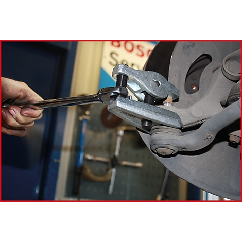 Nahaufnahme eines Mechanikers, der mit einem Schraubenschlüssel und einem Ausdrückwerkzeug an einem Autoreifen arbeitet.